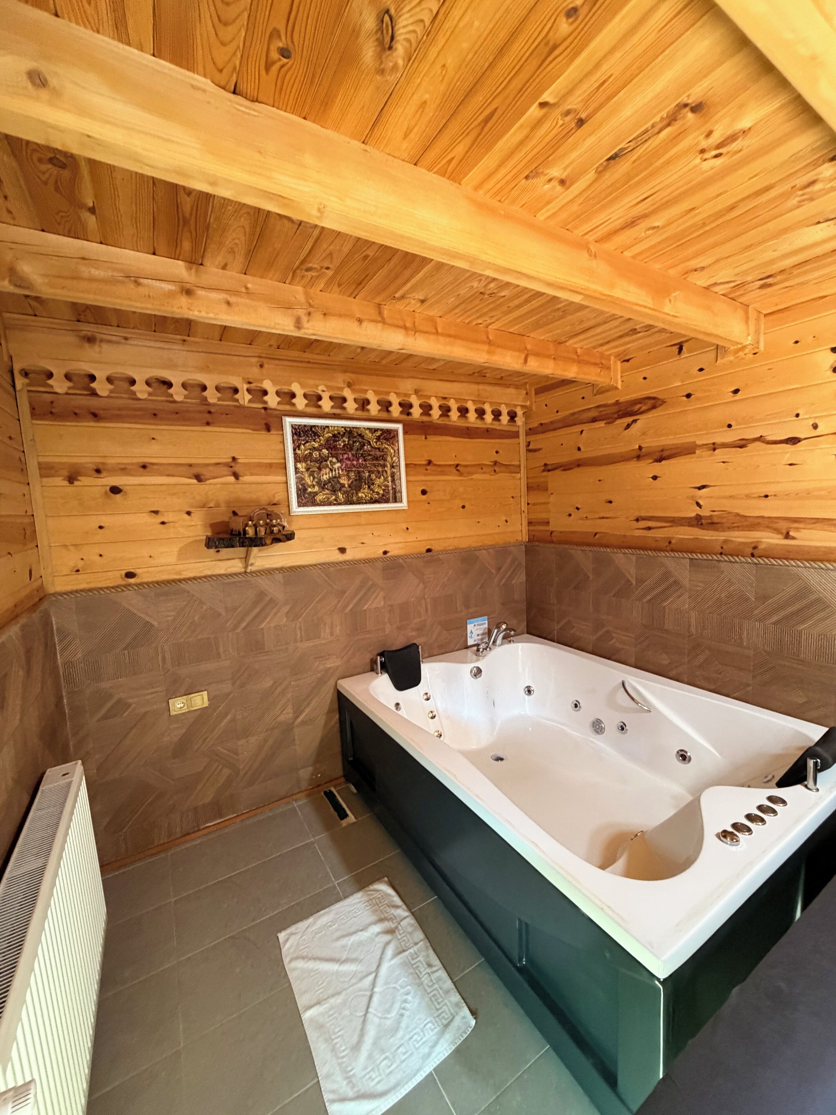 A wooden cabin interior with a large bathtub, a radiator, and a patterned wall.