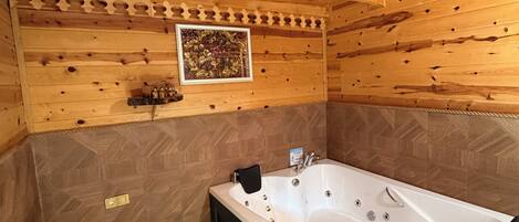 A wooden cabin interior with a large bathtub, a radiator, and a patterned wall.