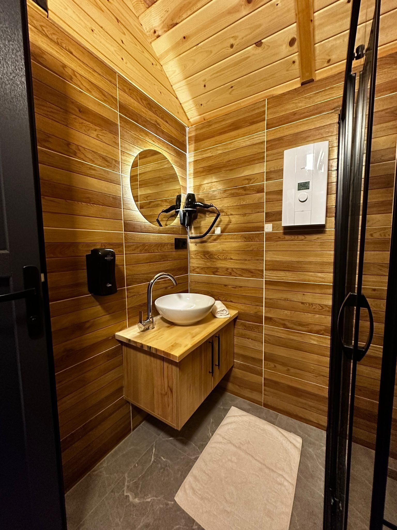 A wooden-paneled bathroom with a sink, mirror, towel, and a digital thermostat.