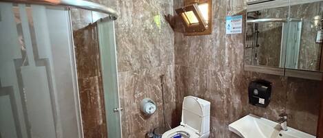 A bathroom with a shower, toilet, sink, and marble walls.