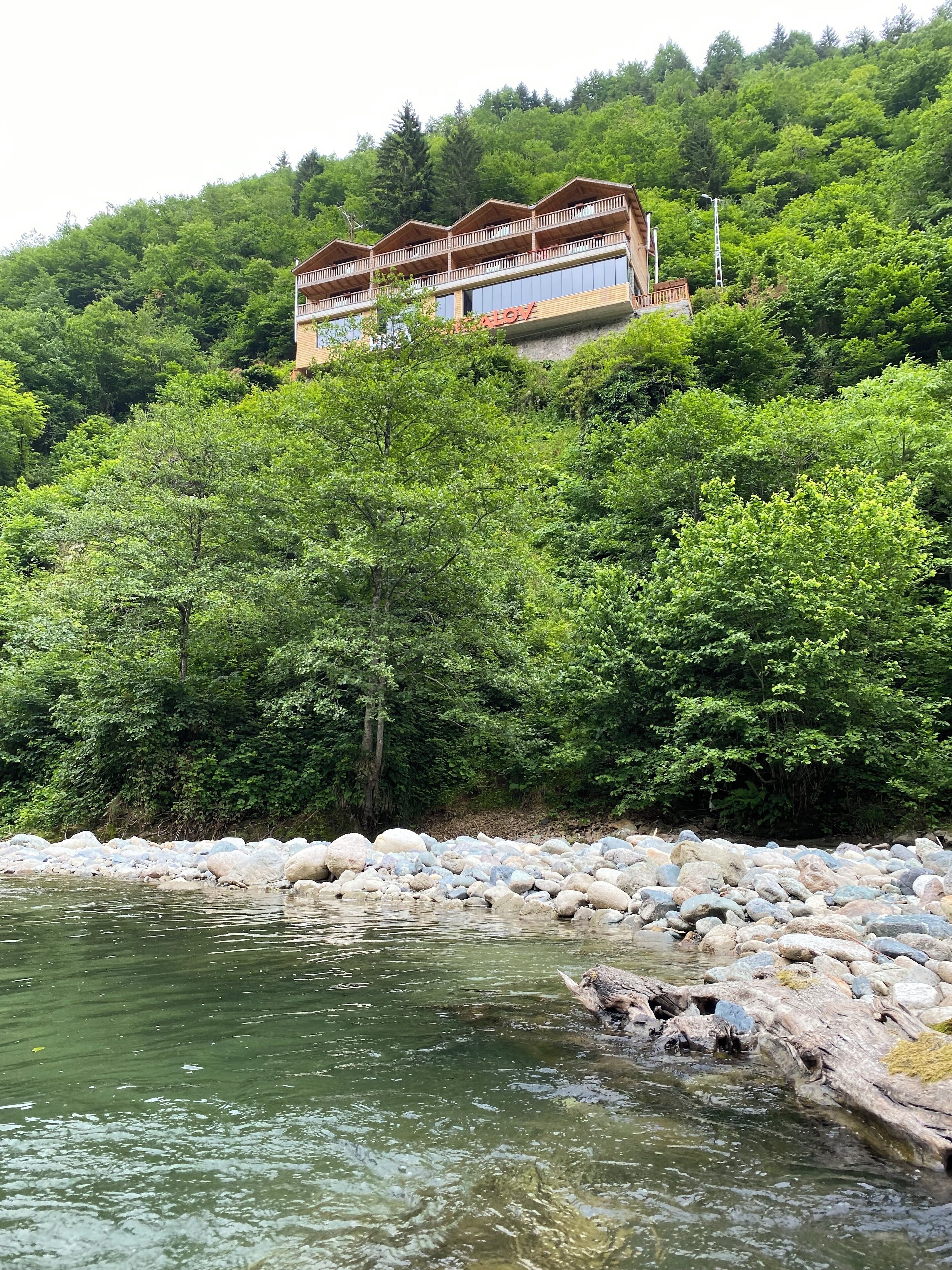 A hotel with a wooden exterior, multiple balconies, and a view of a river surrounded by dense greenery.