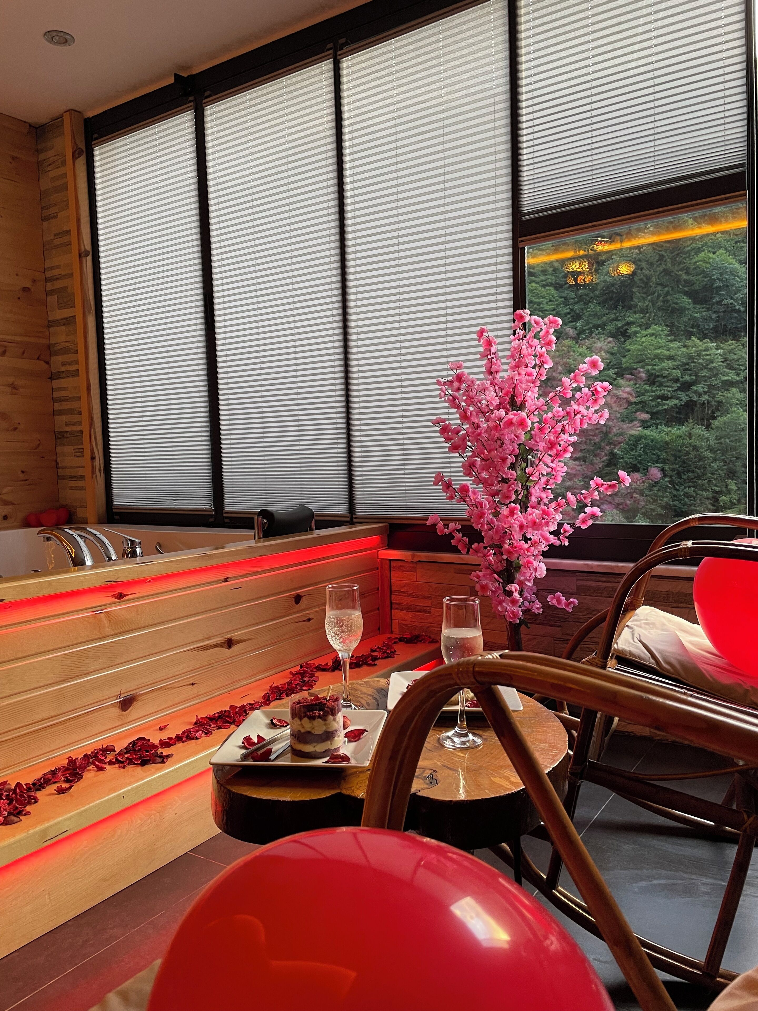 A spa room with a wooden bench, a glass of champagne, rose petals, and a vase of pink flowers.