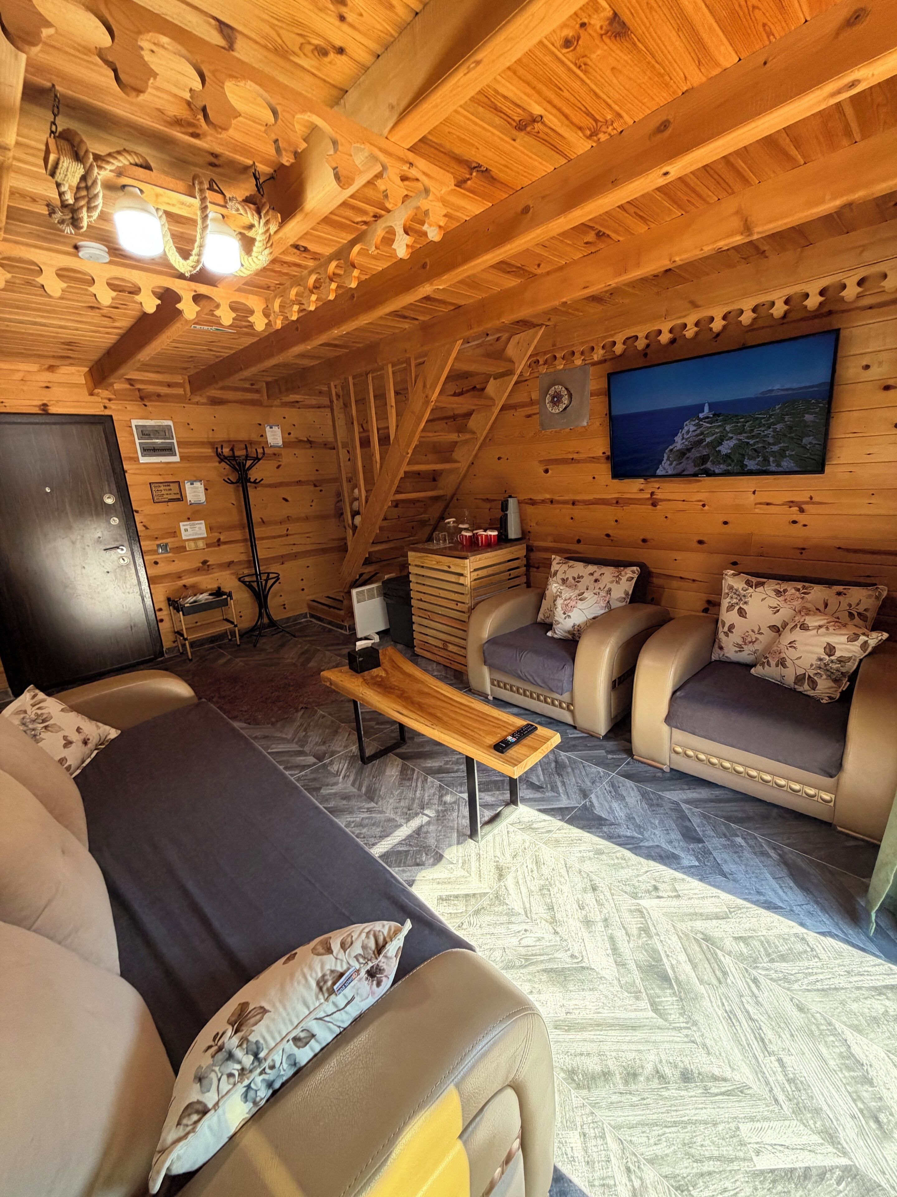 A cozy cabin interior with a sofa, a wooden bench, a television, and a coat rack.