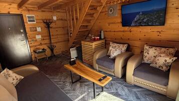 A cozy cabin interior with a sofa, a wooden bench, a television, and a coat rack.