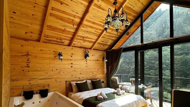 A wooden cabin with a large bed, a separate sleeping area, a bathtub, and a dining table. - Hira Bungalov (Camlihemsin)