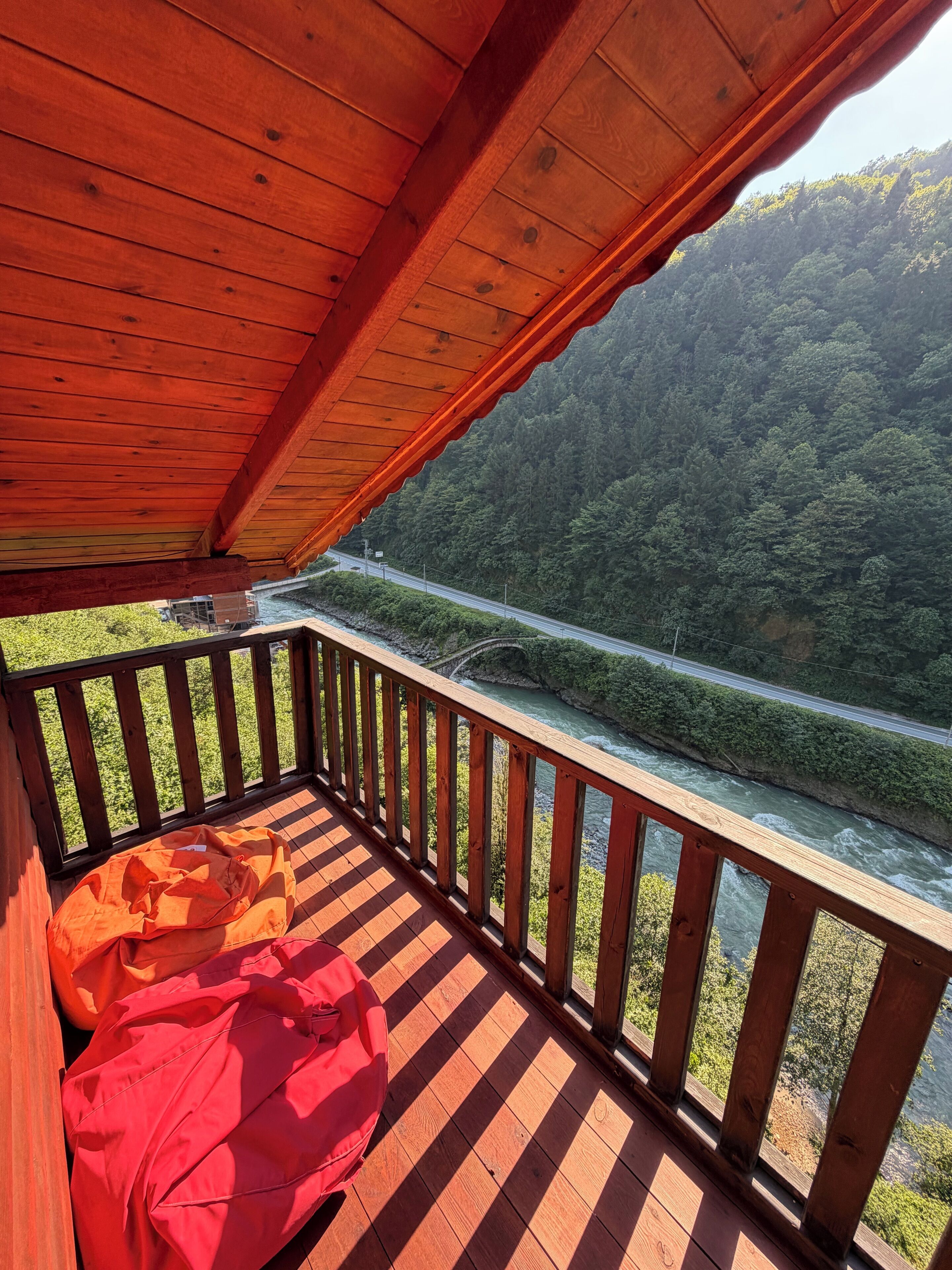 A wooden deck with a checkered floor, a red bag, and a view of a river and forested hills.