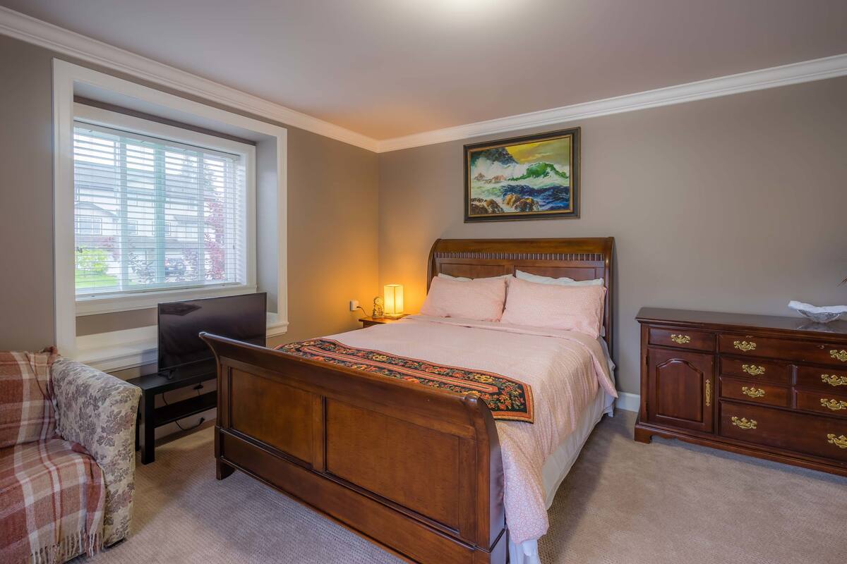 Een slaapkamer met een bed, een kaptafel, een televisie en een raam met jaloezieën.
