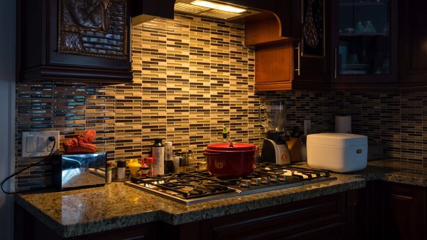 Una cocina con salpicadero de azulejos, encimera de granito y una olla roja en la estufa.