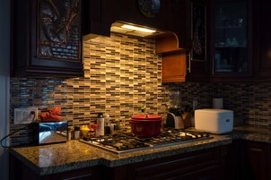 Una cocina con salpicadero de azulejos, encimera de granito y una olla roja en la estufa.