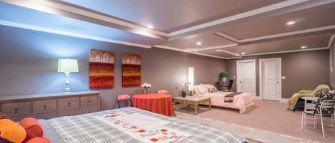 A bedroom with a large bed, a desk, a chair, a table, and two doors.