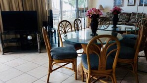 A dining area with a round glass table, six wicker chairs, and a television in the corner. - Special December rates /Spectacular Ocean views 1Bed/2 bath (Kihei)