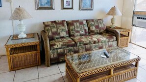 A living room with a sofa, two side tables with lamps, a glass coffee table, and framed pictures on the wall. - Special December rates /Spectacular Ocean views 1Bed/2 bath (Kihei)