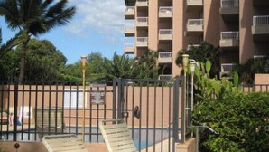 A multi-story building with balconies, a gated entrance, and a pool area with lounge chairs. - Special December rates /Spectacular Ocean views 1Bed/2 bath (Kihei)