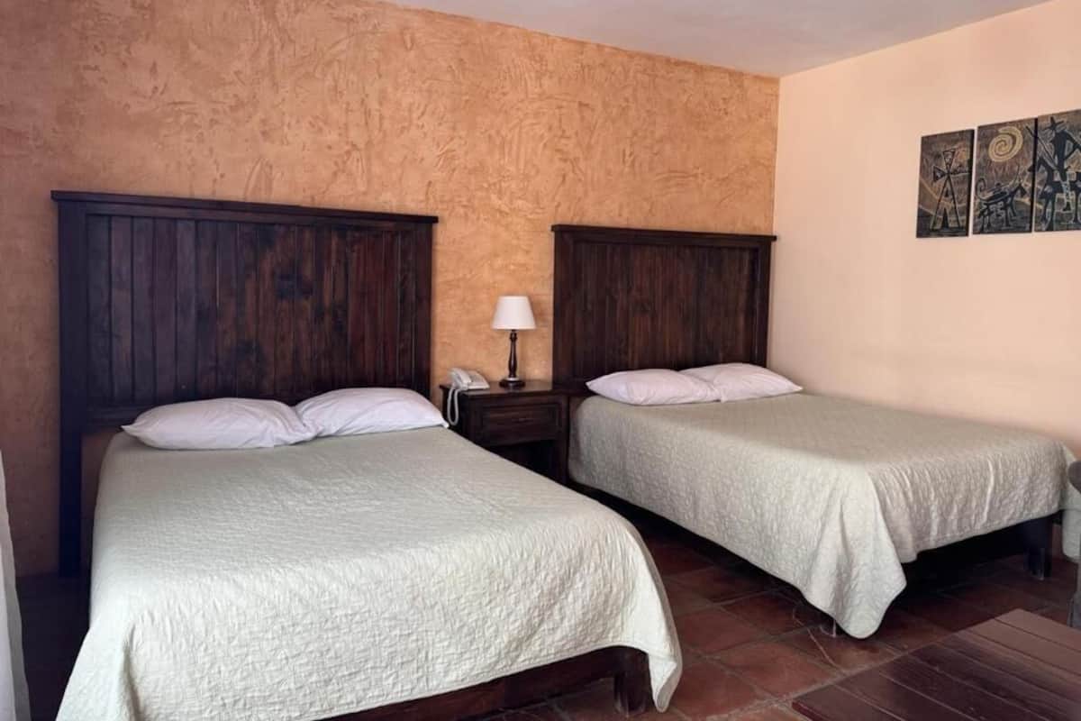 A room with two beds, a nightstand with a lamp, and a wall with artwork.