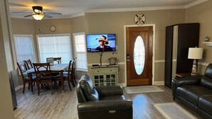 A living room with a leather sofa, a dining area with a table and chairs, a television, a door with a glass panel, and a ceiling fan. - Comfortable 3 BR / 2 Bath n convenient location (Myrtle Beach)