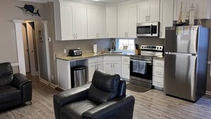 A modern kitchen with white cabinets, stainless steel appliances, a black leather chair, and a wooden floor. - Comfortable 3 BR / 2 Bath n convenient location (Myrtle Beach)