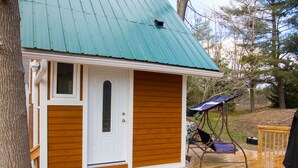 Una pequeña cabaña de madera con techo de chapa verde, una puerta principal y un porche con una mecedora.