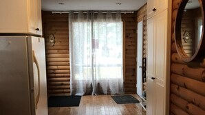 Cocina de estilo cabaña de madera con pisos de madera, un refrigerador, una ventana con cortinas y una puerta con espejo.