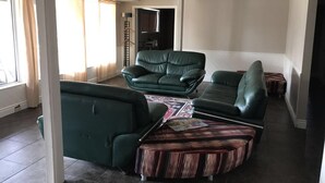 Un amplio salón con un sofá verde, un reposapiés estampado y vistas a otra habitación a través de un arco abierto.