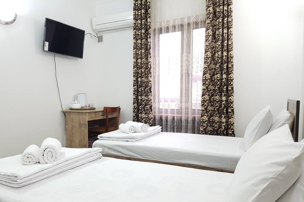A hotel room with two beds, a desk with a chair, a TV, and an air conditioner.