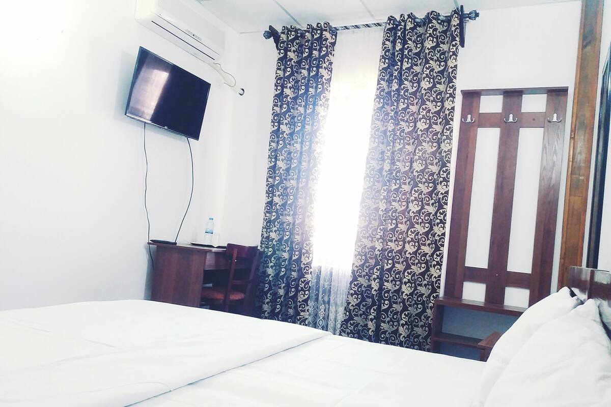 A hotel room with a bed, a desk, a TV, and curtains.