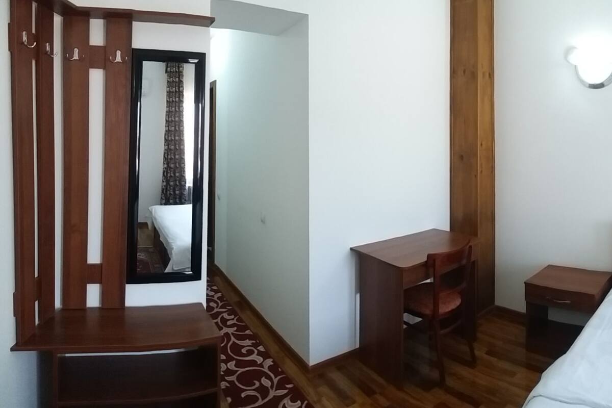 A bedroom with a bed, two bedside tables, a mirror, a wardrobe, and a window with curtains.