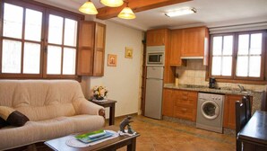 A cozy living room with a sofa, a coffee table, and a kitchen area featuring wooden cabinets, a washing machine, and a refrigerator.