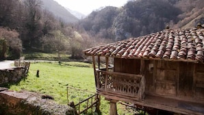 A rustic wooden building with a tiled roof, surrounded by a lush green valley and mountains in the background.