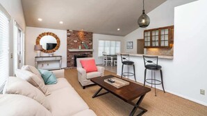Una sala de estar con sofá, mesa de centro y una cocina con taburetes de bar.