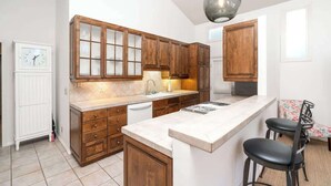 Una cocina con armarios de madera, encimera blanca, un lavamanos y una zona de bar con dos taburetes.