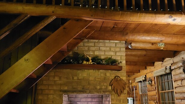 L’intérieur d’une cabane en rondins, avec une cheminée, des poutres en bois et un téléviseur.