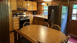 Une cuisine rustique aménagée dans une cabane en bois, avec une table à manger, des chaises, un réfrigérateur, une cuisinière et une machine à café.