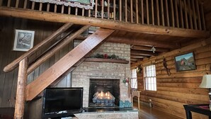 L’intérieur d’un chalet rustique, avec un escalier en bois, une cheminée, un téléviseur et un coin salon confortable.