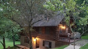 Un chalet rustique en rondins de bois, doté d’une terrasse, de meubles de jardin et d’un foyer extérieur.