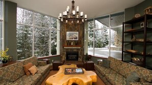 A cozy living room with a fireplace, large windows, and a wooden coffee table. - Woodrun Lodge condo w/ pool & hot tub (Whistler)