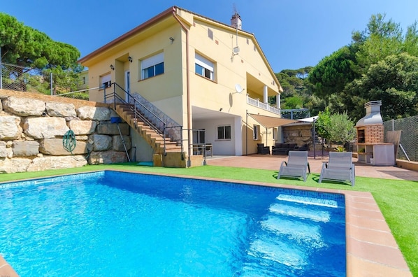 A two-story house with a swimming pool, outdoor seating, and a stone wall.