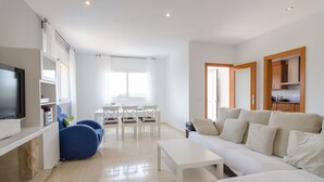 A modern living room with a sofa, a TV, a dining table with chairs, and a kitchen area visible through an open door. - Club Villamar - Precious villa with private pool located in a residential area, a perfect electio... (Lloret de Mar)