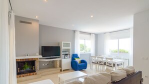 A modern living room with a fireplace, a flat-screen TV, a dining area with a table and chairs, and a large window providing natural light. - Club Villamar - Precious villa with private pool located in a residential area, a perfect electio... (Lloret de Mar)