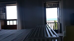Une chambre avec un lit, une fenêtre donnant sur la mer et un balcon avec une balustrade.