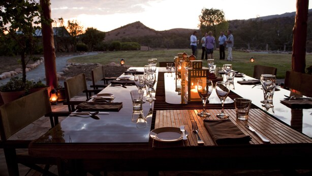 An outdoor dining area with tables set for a meal, surrounded by natural scenery and hills in the background. - Arkaba Homestead (Hawker)