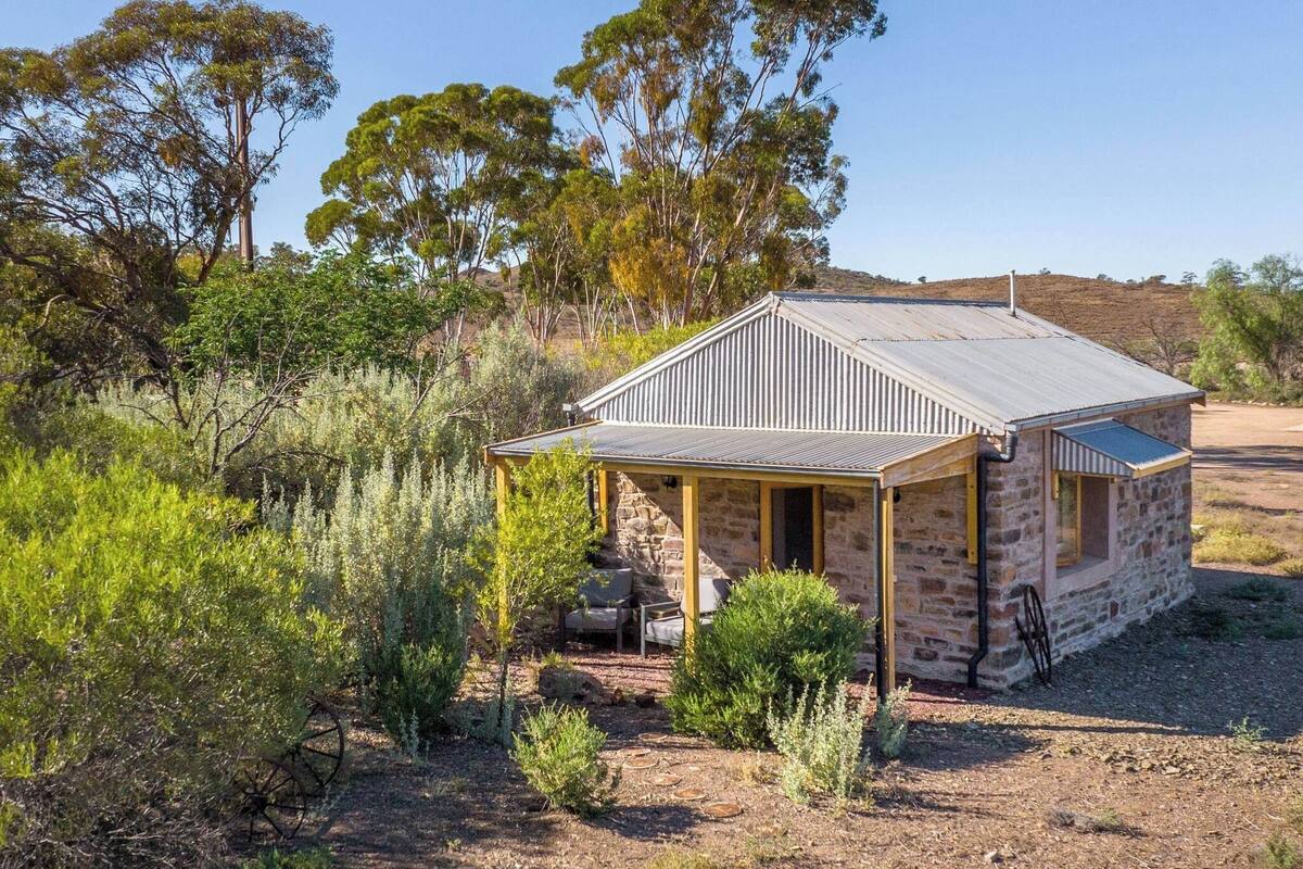 A stone building with a corrugated metal roof, surrounded by native vegetation and trees.