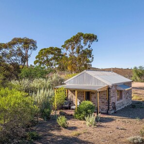 A stone building with a corrugated metal roof, surrounded by native vegetation and trees.