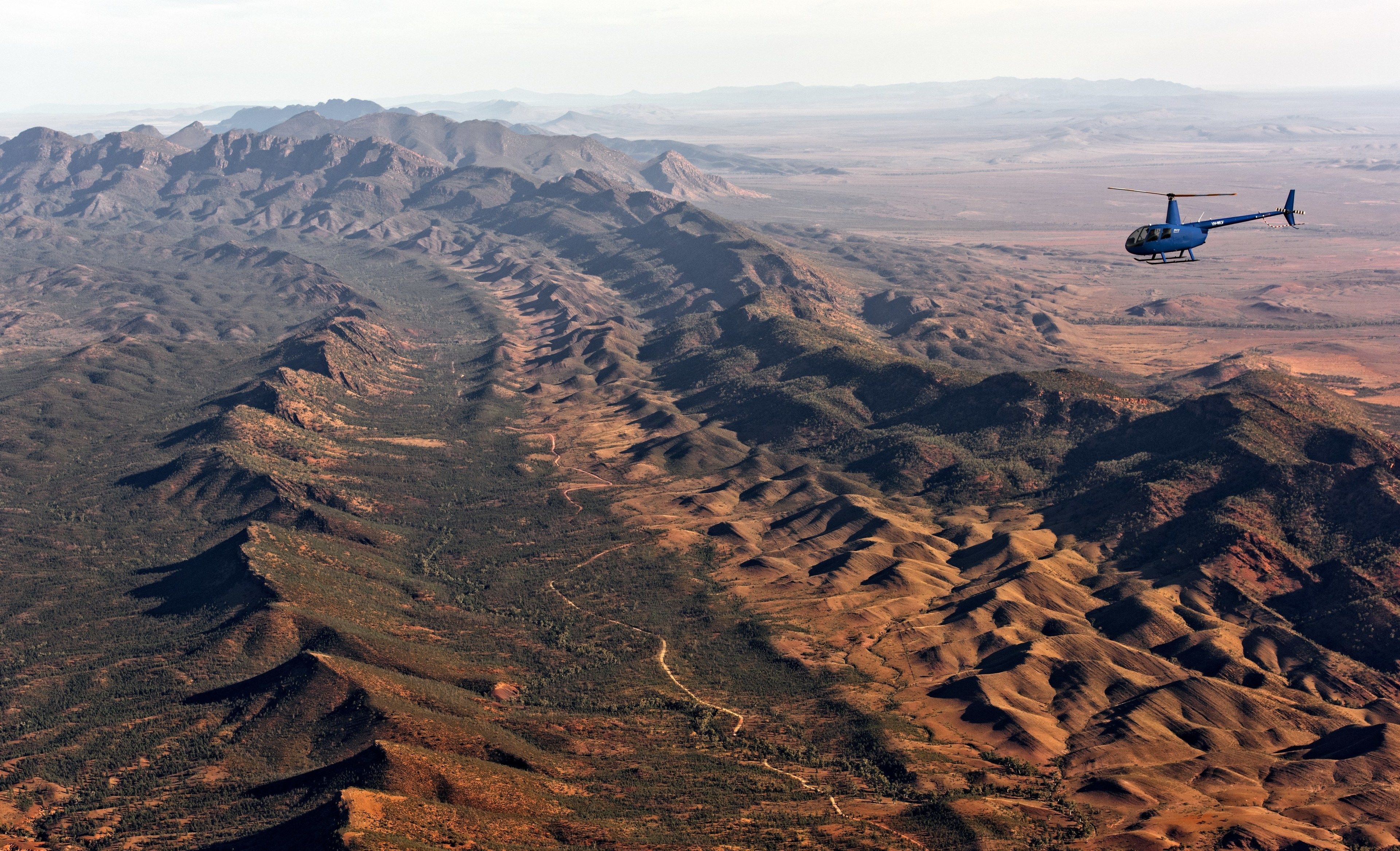 A helicopter flying over rugged terrain with a clear view of the landscape below.