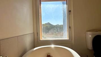 A bathroom with a bathtub, a window, and a wooden drying rack.