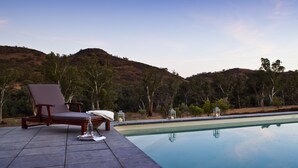 A poolside area with a lounge chair and a table, surrounded by a hilly landscape. - Arkaba Homestead (Hawker)
