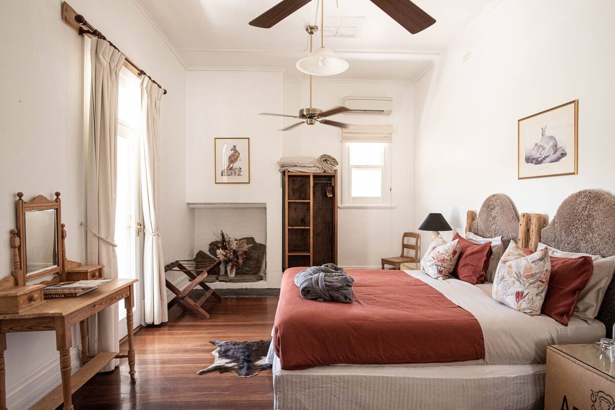 A bedroom with a wooden bed, a ceiling fan, a fireplace, and a dog on the floor.