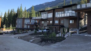 A modern multi-story building with large windows and balconies, surrounded by a forest and mountains. - New built, modern ski-in/ski-out home with great views of Columbia River Valley (Golden)