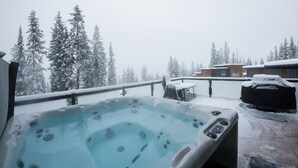 A hot tub on a snowy deck with a view of snow-covered trees and a building in the background. - New built, modern ski-in/ski-out home with great views of Columbia River Valley (Golden)
