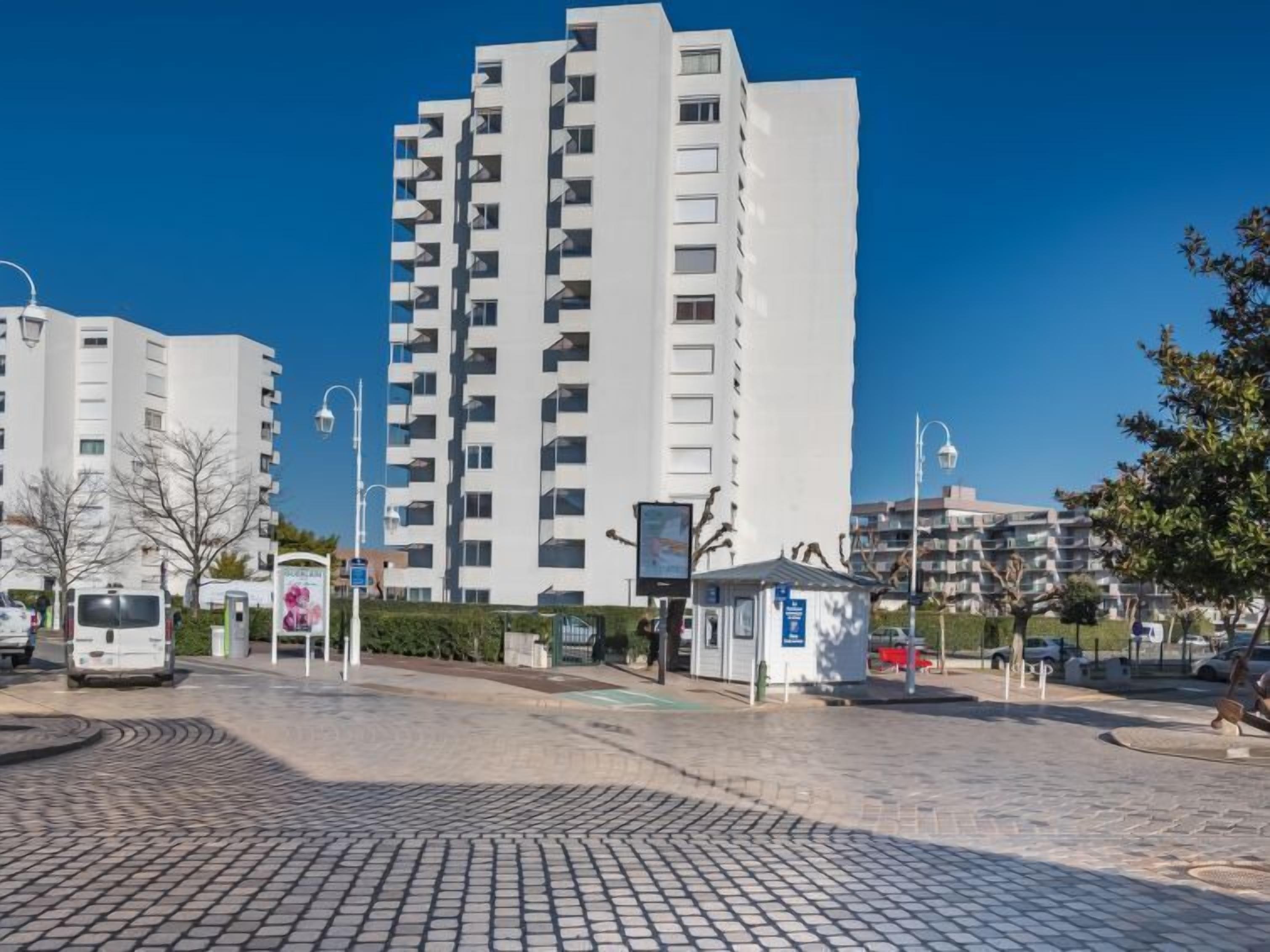 A modern apartment building with multiple balconies, a paved plaza, and a small kiosk.
