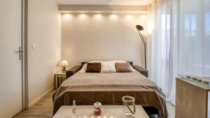 Et moderne hotelværelse med en stor seng, sengeborde med lamper, et lille bord med stearinlys og udsigt til det fri.